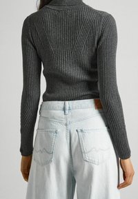 Grå ribbad stickad topp med hög krage, med långa ärmar. Matchad med ljusblå denimjeans med sydda fickdetaljer.