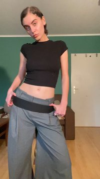 Svart avkortet topp og grå vide bukser med svart liv. Rom med grønne vegger og en dør i bakgrunnen.