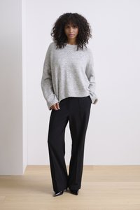 Grijze gebreide trui met een relaxte pasvorm, gecombineerd met hoge zwarte wijde broek. De outfit heeft lange mouwen en puntige zwarte hakken.