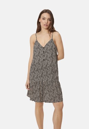 Mujer con vestido sin mangas hasta la rodilla, con estampado en blanco y negro y tirantes finos, de pie contra un fondo claro y liso.