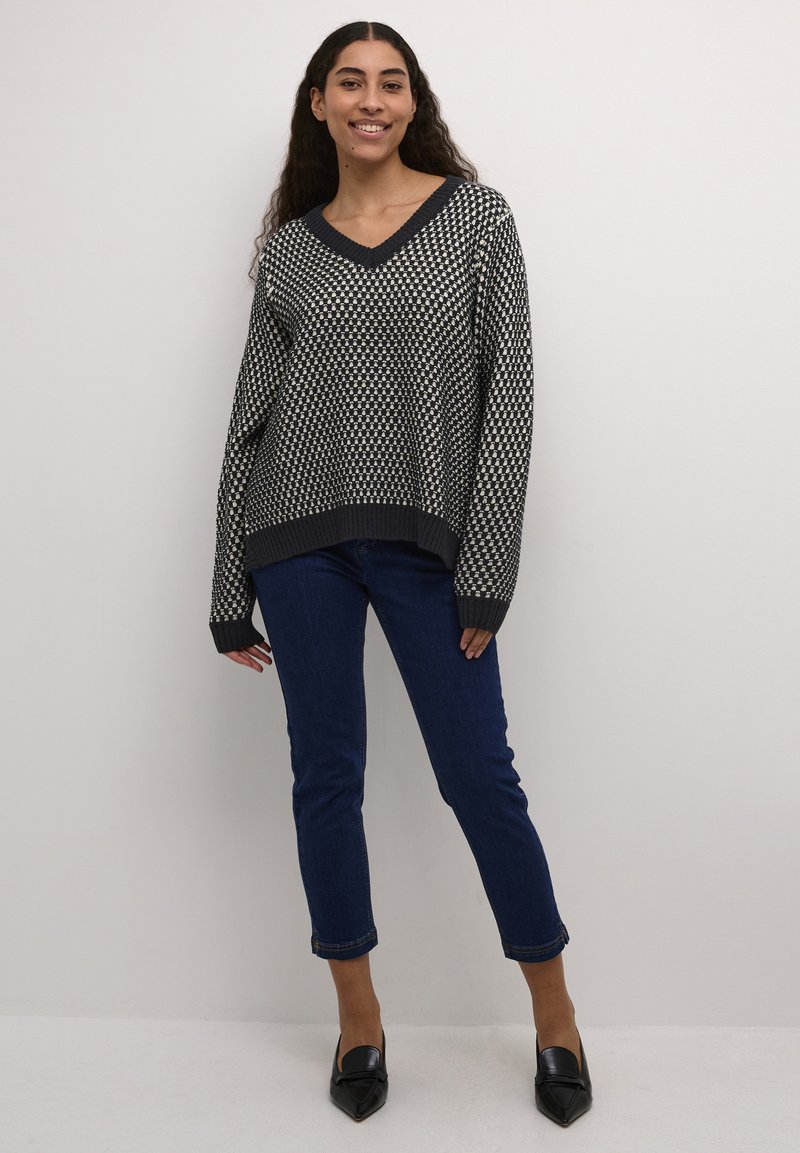 Adīts melnbalts svītrots džemperis ar V veida kaklu, brīvu piegriezumu un ribotām piedurknēm, apvienots ar tumši ziliem ievilktiem džinsiem un melniem norādītām kurpēm.