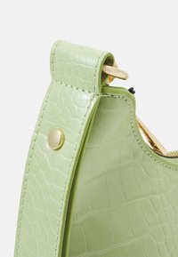 Zielona torebka z ekologicznej skóry o fakturze krokodyla, z złotymi ozdobami i usztywnionym kształtem z uchwytem u góry.