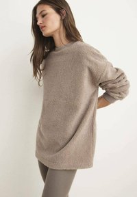 Beige fleecetrui met een gestructureerde afwerking, verlaagde schouders en een geribbelde halsband, gecombineerd met fitted, neutraalgekleurde leggings.