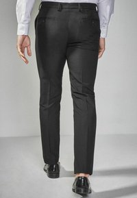Čierne šité nohavice s úzkym strihom, vybavené bočnými vreckami a gombíkovými zadnými vreckami. Hladká látka s jemným leskom.