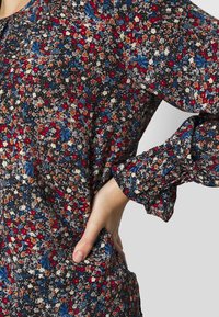 Svart blommig klänning med röda, vita och blå blommor; har rynkade långa ärmar och en avslappnad passform. Mjuk tyg och intrikata mönsterdetaljer.