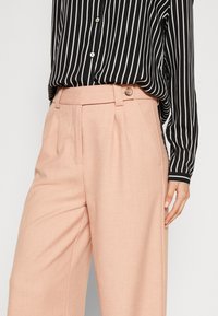 Světle růžové přizpůsobené kalhoty se bočními kapsami, záhyby a zapínáním na knoflík, spárované s černobílou pruhovanou košilí na knoflíky.