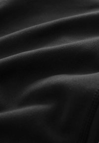 Schwarzer Stoff mit glatter Textur, der subtile Falten und ein mattes Finish aufweist, und eine uniforme, tiefe Farbe ohne Muster oder Akzente zeigt.