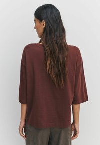 Brown oversized t-shirt with short, wide sleeves, featuring a rounded neckline and a relaxed fit. Textured fabric detail visible.