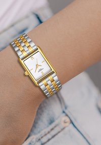 Reloj rectangular con una esfera texturada blanca, acentos en oro y una pulsera metálica en plata y oro con eslabones alternos.
