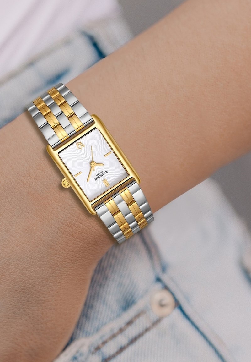 Reloj rectangular con una esfera texturada blanca, acentos en oro y una pulsera metálica en plata y oro con eslabones alternos.