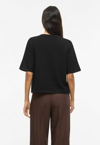 Mustast lühikeste varrukatega särk ümmarguse kaelusega, millel on lõdvestunud lõige ja sile tekstuur, sobitatud pruunide laiade pükstega.