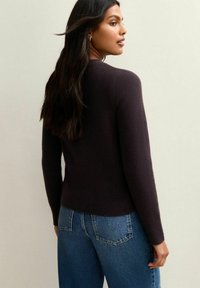 Maglione lavorato a maglia di un viola scuro con scollatura rotonda e maniche lunghe, abbinato a jeans blu a vita alta, mostrato di spalle.