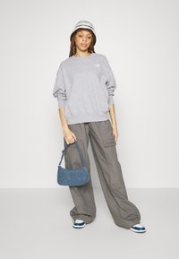 Felpa grigia, pantaloni cargo grigi larghi, borsa in denim blu e scarpe da ginnastica con dettagli blu. Il modello indossa un cappello a secchiello a righe.
