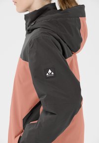 Wasserabweisende Jacke mit einem Farbblockdesign in Dunkelgrau und Koralle, aus strapazierfähigem Stoff und mit einem Logo-Patch auf dem Ärmel.