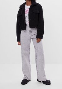 Czarna, strukturalna krótka kurtka z zapięciem na guziki i dwoma kieszeniami na piersi, w połączeniu z jasnoszarymi spodniami o szerokich nogawkach i czarnymi butami na platformie.