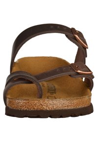 Brun lædersandal med to justerbare stropper, kobber spænder og en tekstureret korksål. Flad sål med mønstret greb for trækkraft.