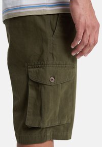 Olijfgroene cargoshorts van zacht materiaal, met een zijflapzak met een knoop en zichtbare stiksels op de zoom.