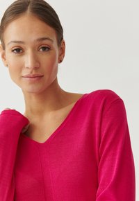 V-Ausschnitt-Pullover in leuchtendem Pink, aus einem weichen Strickstoff gefertigt. Lange Ärmel mit eng anliegenden Manschetten und einem nahtlosen Design.