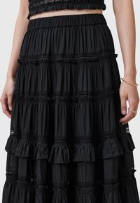 Jupe noire à volants en tissu léger, avec bords volantés, accents en dentelle et taille élastique pour un ajustement confortable.