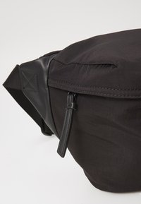 Borse a cintura in tessuto nero con superficie texturizzata, dettagli in pelle e chiusura con zip. Dotata di una tracolla resistente per un indossabilità regolabile.