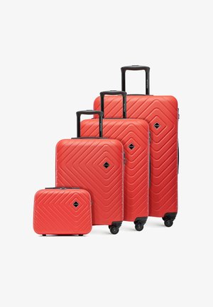 Quattro valigie rigide rosse di diverse dimensioni con manici neri retrattili e ruote, disposte dalla più piccola alla più grande.