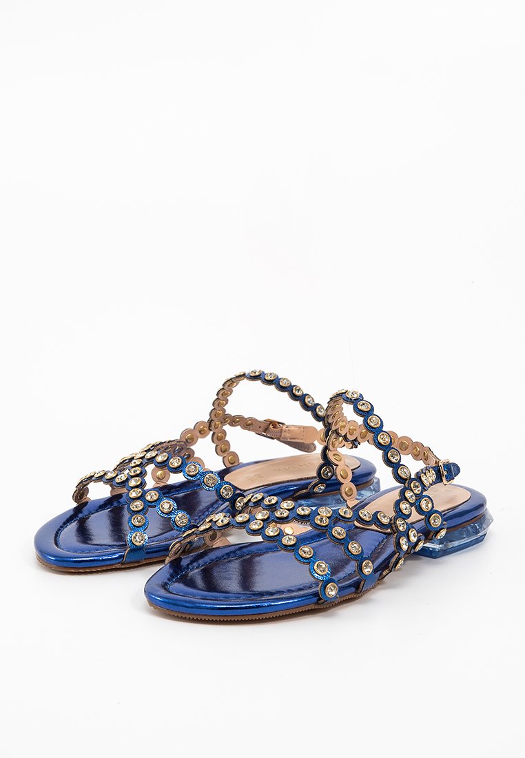 Sandali metallici blu con suola piatta, caratterizzati da un design a strisce decorato con accenti dorati circolari e gemme rotonde.