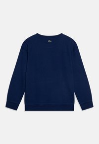 Marinblå sweatshirt i bomull. Har rund hals, långa ärmar och ribbade manschetter. Inkluderar en liten grön logotyp på baksidan av nacklinningen.