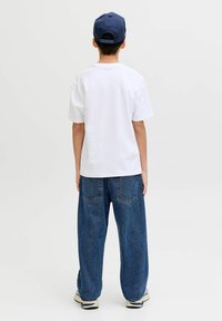 Fehér, rövid ujjú pamut póló, laza szabású kék farmernadrággal és hátul viselt tengerészkék sapkával.