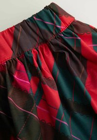 Czerwono-zielona tkanina z wzorem, z marszczonym pasem. Charakteryzuje się wzorem diamentów i kontrastowymi przeszyciami. Gładka faktura.