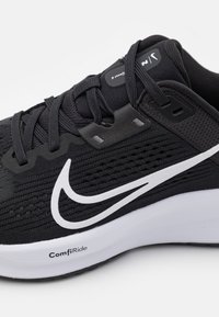 Zwarte sportschoen met een gestructureerde bovenkant, witte Nike swoosh en een gewatteerde witte zool met het label "ComfiRide."