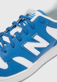 Blauwe en witte sneaker met een gestructureerde leren bovenkant, contrasterende veters, een opvallend wit logo en een rubberen zool met stikdetails.