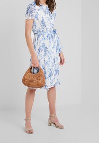 Blommönstrad klänning i vitt och blått, med korta ärmar, knytmidja och volangkant. Styld med en vävd brun väska och beige klackar.