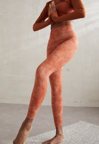 Terracotta athletic leggings with a mottled texture, high waistband, and a body-hugging fit, paired with a coordinating long-sleeve top.