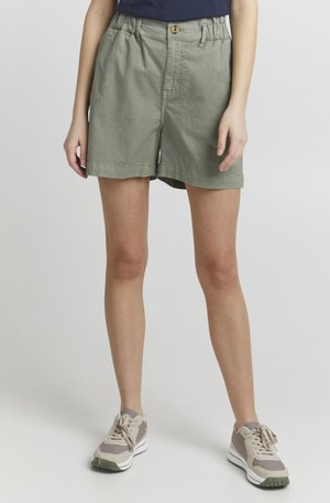 Light green cotton shorts with a relaxed fit, front button closure, and gathered waistband. Paired with beige athletic shoes.
