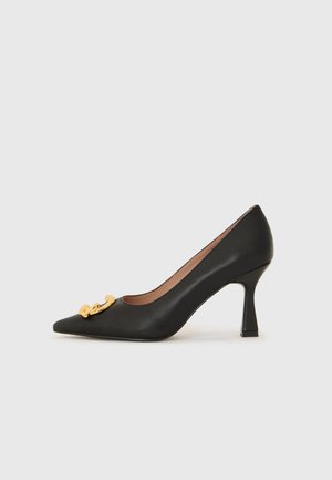 Scarpa nera in pelle con tacco alto, punta affusolata e dettagli decorativi in oro sulla parte anteriore. Il tacco è a forma blocco e di altezza media.