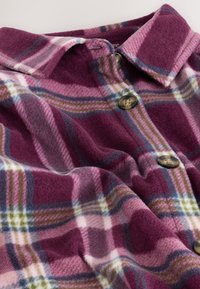 Uldskjorte med krave i lilla og pink ternet mønster med store brune knapper foran.