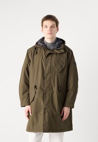 Parka verde-oliva com capuz ajustável, bolso frontal, botões de pressão e forro cinza com padrão. Um ajuste descontraído com mangas longas.