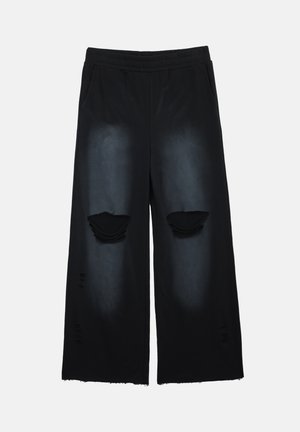 Pantalon noir à jambes larges en tissu doux, avec détails usés, deux poches, et style avec accents déchirés aux genoux.