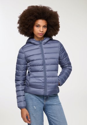 Kurtka puchowa w miękkim niebieskim materiale, z kapturem, zamkiem błyskawicznym z przodu i poziomym wzorem pikowania dla lepszej izolacji. Połączona z jasnoniebieskimi dżinsami.