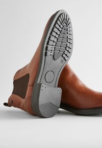 Brown leather ankle boots with a textured finish, mesh side panels, and a rubber sole featuring a traction pattern. Size labeled as 42.