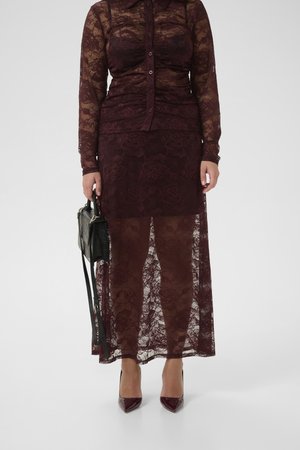 Burgundy lace dress with a buttoned shirt collar, long sleeves, and sheer skirt. Paired with a black handbag and burgundy high heels.