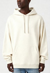Felpa colore crema realizzata in tessuto morbido, con tasca frontale, cappuccio regolabile con coulisse e polsini a costine. Vestibilità oversized con macchie.