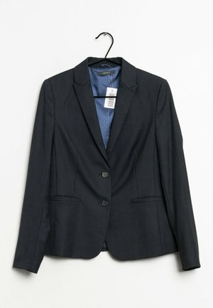 Veste blazer noire pour femmes, cintrée, à deux boutons, avec des revers crantés et une doublure bleue à pois, suspendue à un cintre noir avec une étiquette de prix.