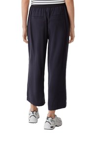 Navyblauwe cropped broek met een relaxte pasvorm, elastische tailleband en twee achterzakken, gedragen met witte sportschoenen. Glad, lichtgewicht materiaal.