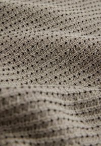 Tejido texturizado de color beige claro con un patrón de malla, que presenta pequeños agujeros y una apariencia suave y tejida. Adecuado para prendas ligeras.