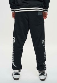 Zwarte joggers met witte grafische prints, elastische tailleband en gestreepte boorden. Gladde stof met NFL-branding en logo-accenten.