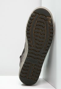 Brauner Lederstiefel mit einer strukturierten Sohle, die ein Zickzackmuster aufweist. An der Seite befindet sich ein Reißverschluss für einen einfachen Zugang. Markenlogo auf der Sohle sichtbar.