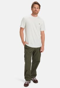 Lys grå spraglet t-shirt med korte ærmer, parret med olivengrønne cargo-bukser med sidelommer, iført brune og hvide sneakers.