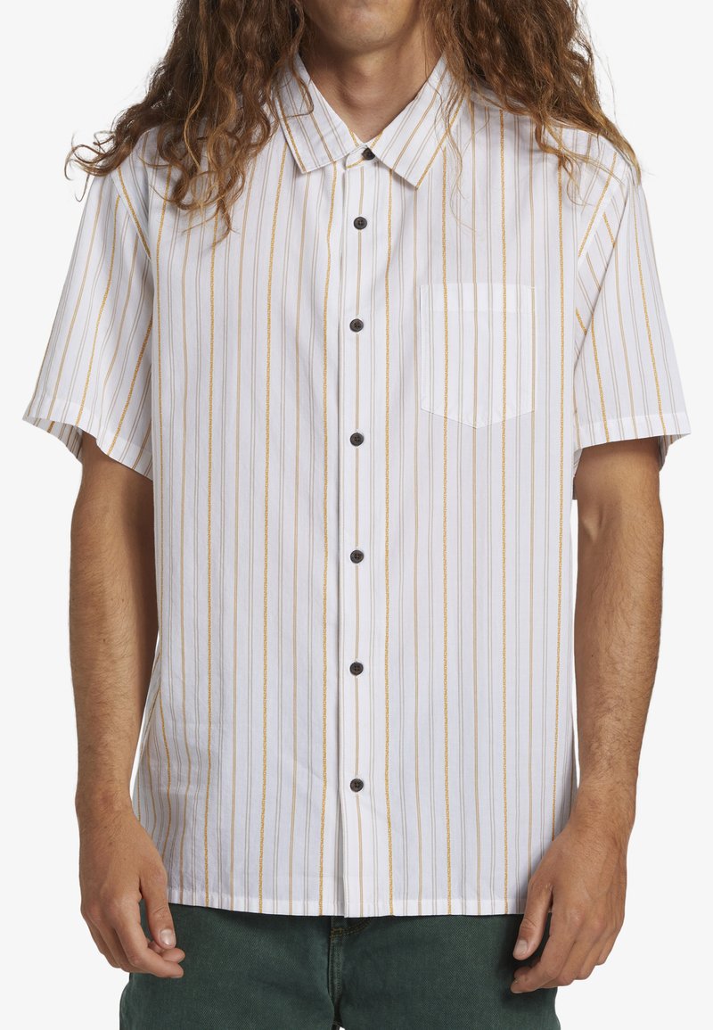Chemise à manches courtes à boutons de couleur blanche avec des rayures verticales jaunes, dotée d'une poche poitrine et de boutons noirs. Tissu en coton, coupe décontractée.