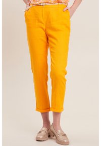 Orangene Leinenhosen mit entspanntem Schnitt, umgeschlagenen Säumen und glatter Textur, kombiniert mit hellen Mokassins.